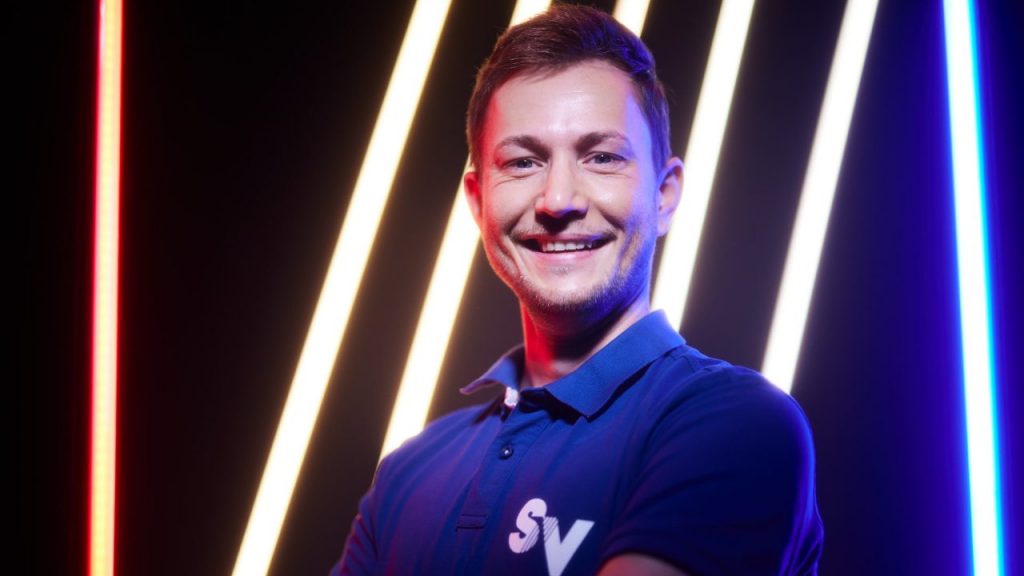 Mitarbeiter Maik in blauem Spandauer Velours-Shirt, dahinter Neonbeleuchtung