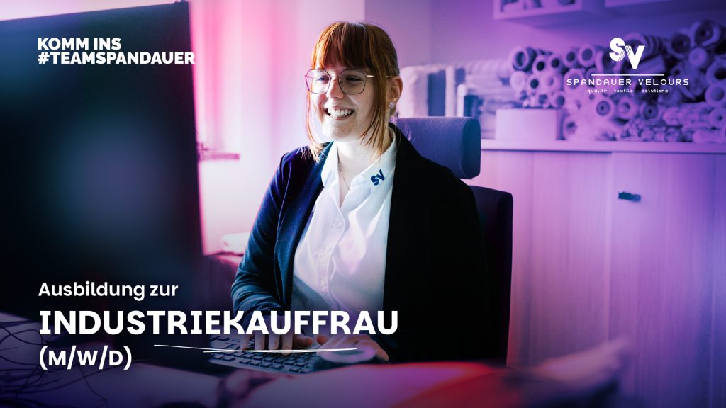 Junge Frau sitzt fröhlich lächelnd vor ihrem Monitor im Büro.