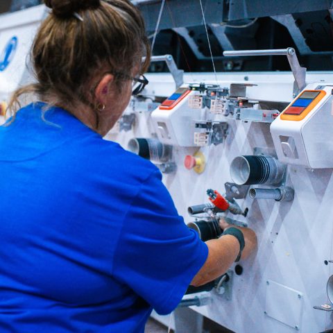 Arbeiterin von hinten bei der Bedienung und Wartung einer Garnwickelmaschine in der Spinnerei