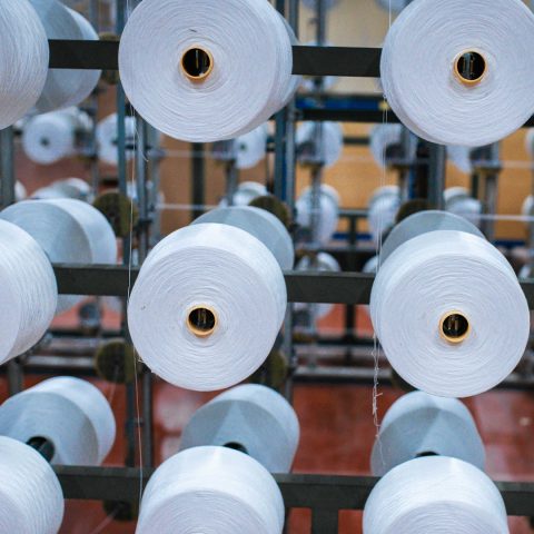 Detaillierte Aufnahme vieler aufgehängter, großer, weißer Garnrollen an einer industriellen Halterung.
