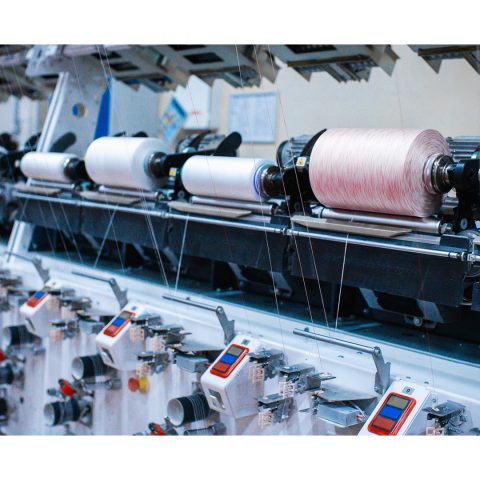 Industrielle Spulmaschine mit weißen und leicht roséfarbenen Garnspulen während des Betriebs.