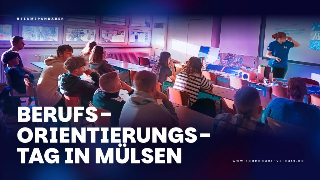 Eine Dozentin von Spandauer Velours hält einen Vortrag zur Berufsorientierung für Schüler in einem Klassenzimmer der Oberschule Mülsen. Der Text im Vordergrund lautet: "BERUFSORIENTIERUNGSTAG IN MÜLSEN", zur Bewerbung von Ausbildungs- und Karrieremöglichkeiten.