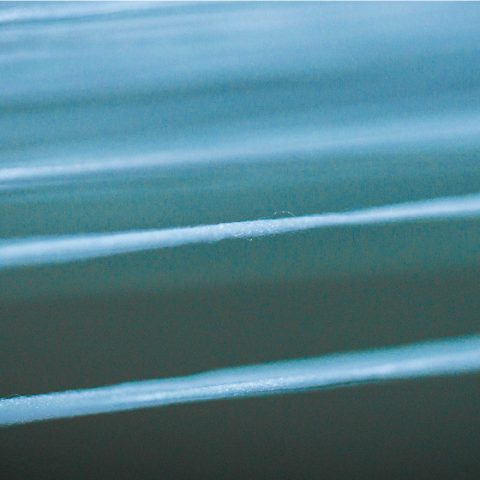 Makroaufnahme von fein gespannten, hellblauen Garnen in einer Weberei zur Verdeutlichung der präzisen Textilverarbeitung.