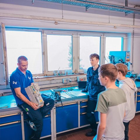 Ein Ausbilder von Spandauer Velours erklärt einer Gruppe von interessierten Jugendlichen technische Bauteile in der Lehrwerkstatt während eines Schnuppertages.