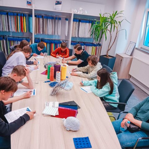 Workshop-Atmosphäre bei der Berufsberatung: Jugendliche sitzen an einem Tisch mit Textilproben und Garnrollen bei Spandauer Velours und bearbeiten Informationsbögen.