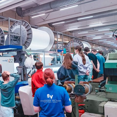 Werksführung für Schüler durch die Produktionshalle von Spandauer Velours mit Blick auf große Textilmaschinen und industrielle Webanlagen.
