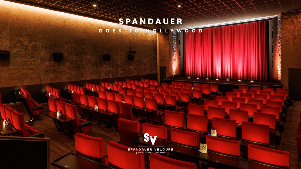 Moderner Kinosaal mit roten Samtsesseln, der Wandbespannung Virginia, und Vorhang Viola von Spandauer Velours – Referenzprojekt.Der Spruch „Spandauer goes to Hollywood“ steht auf dem Bild.
