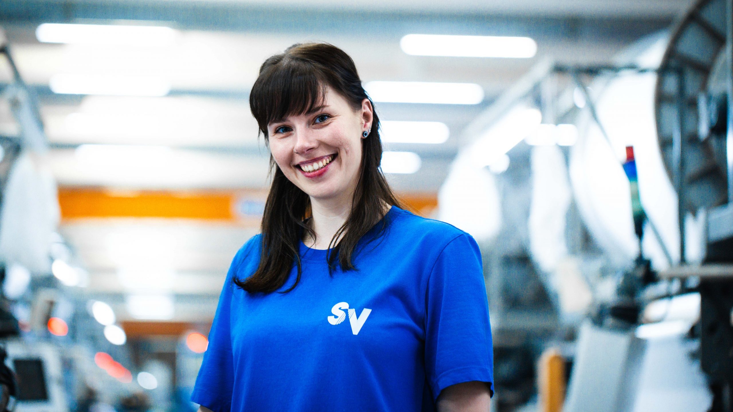 Maschinen- und Anlagenführerin Jasmin an ihrem Arbeitsplatz lächelt freundlich in die Kamera.