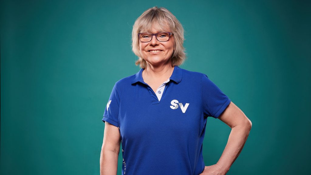 Mitarbeiterin Christina lächelt freundlich in blauem Spandauer Velours-Shirt in die Kamera.