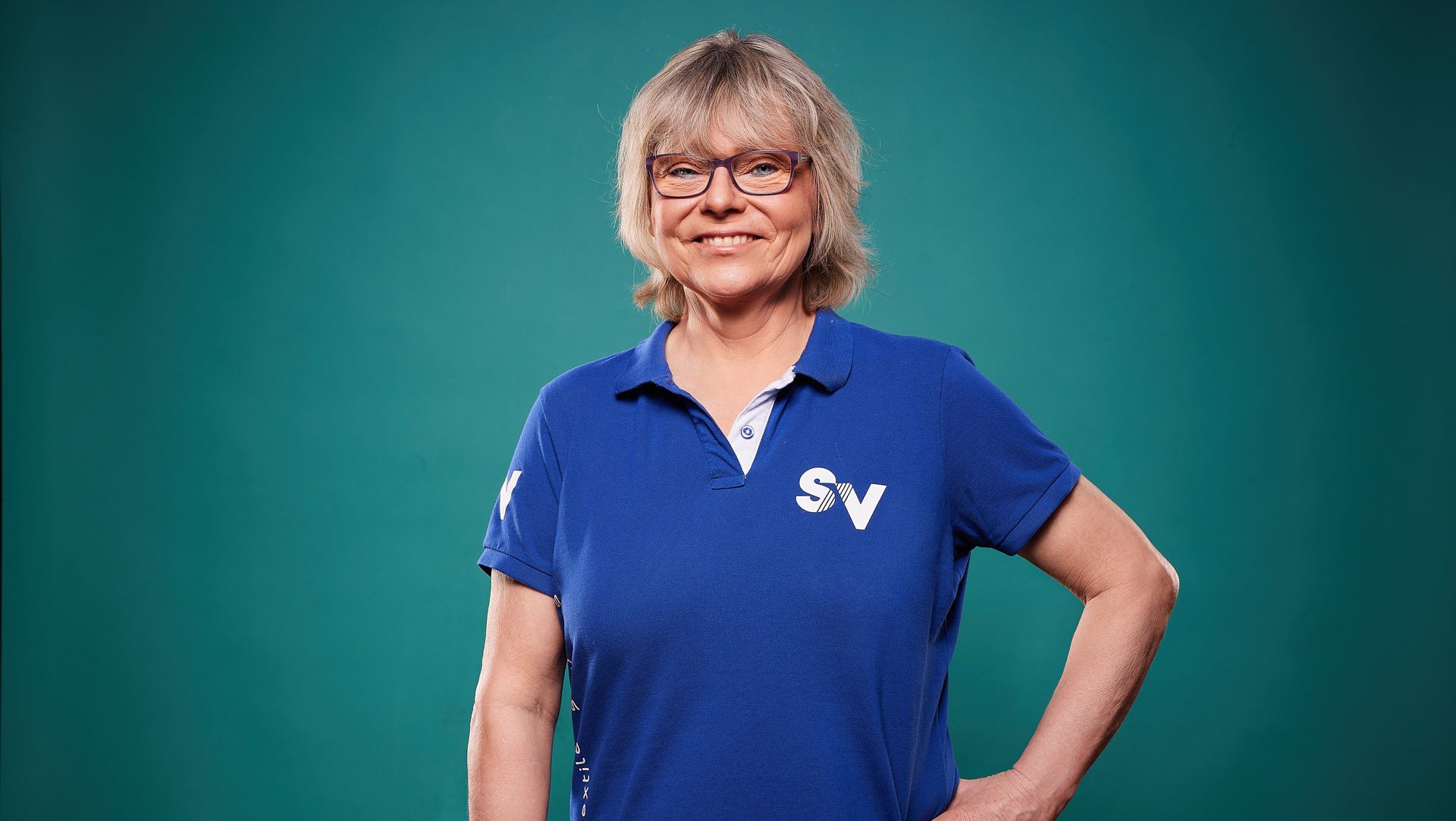 Mitarbeiterin Christina lächelt freundlich in blauem Spandauer Velours-Shirt in die Kamera.