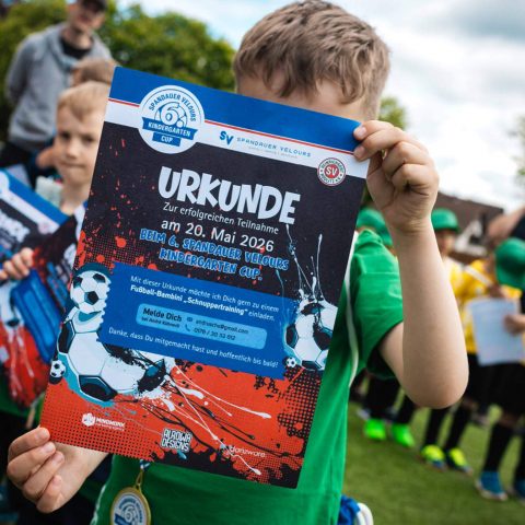 19. Ein Kind im grünen Trikot hält stolz eine Urkunde zur erfolgreichen Teilnahme am Spandauer Velours Kindergarten Cup in die Kamera.