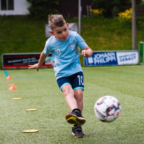 9. Ein Junge im hellblauen Trikot mit der Nummer 10 schießt beim Elfmeterschießen schwungvoll den Fußball in Richtung Tor.