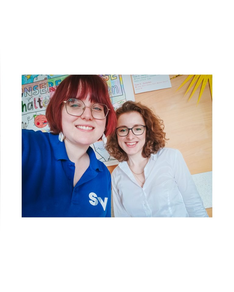 Zwei lächelnde Mitarbeiterinnen der Spandauer Velours im blauen Firmen-Poloshirt und weißer Bluse beim Ausbildungsevent an der Schule.