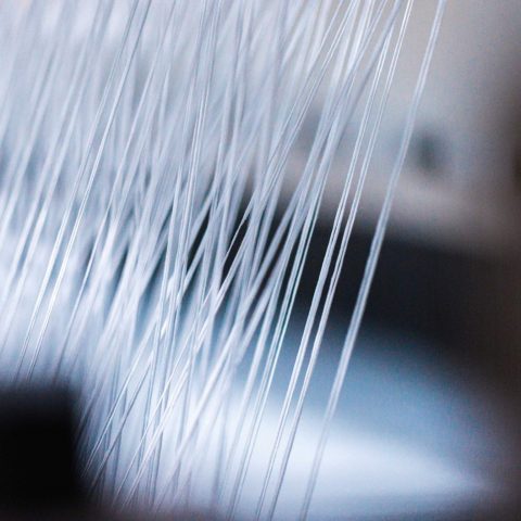 Detailaufnahme von fein aufgespannten, weißen Garnfäden auf einer industriellen Webe-Maschine bei Spandauer Velours.