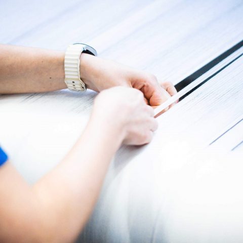 Präzise Qualitätskontrolle: Hände einer Textilfachkraft führen feinste Fäden durch den Kalander-Prozess bei Spandauer Velours.